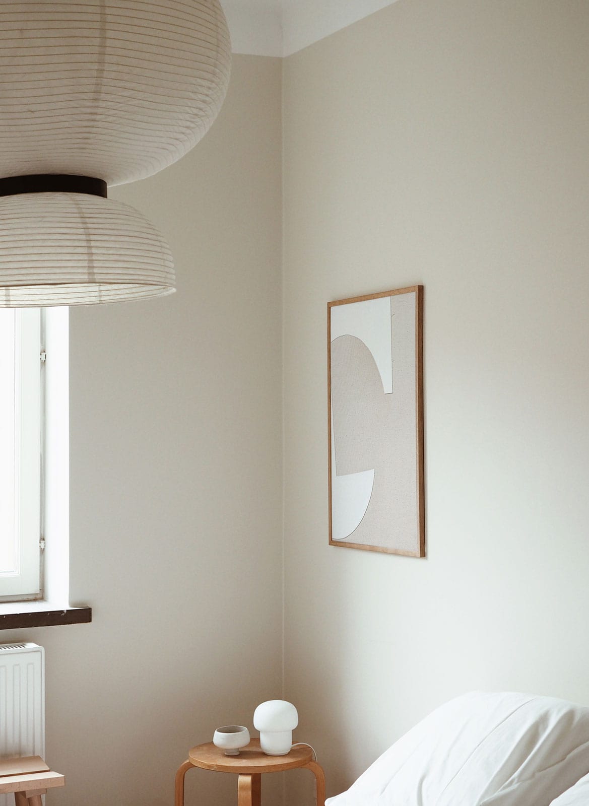Framed white on white poster hanging in bedroom by Atelier Cph