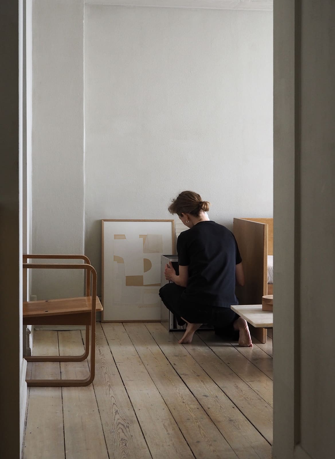 Framed minimalistic poster standing in a living room with a person by Atelier Cph