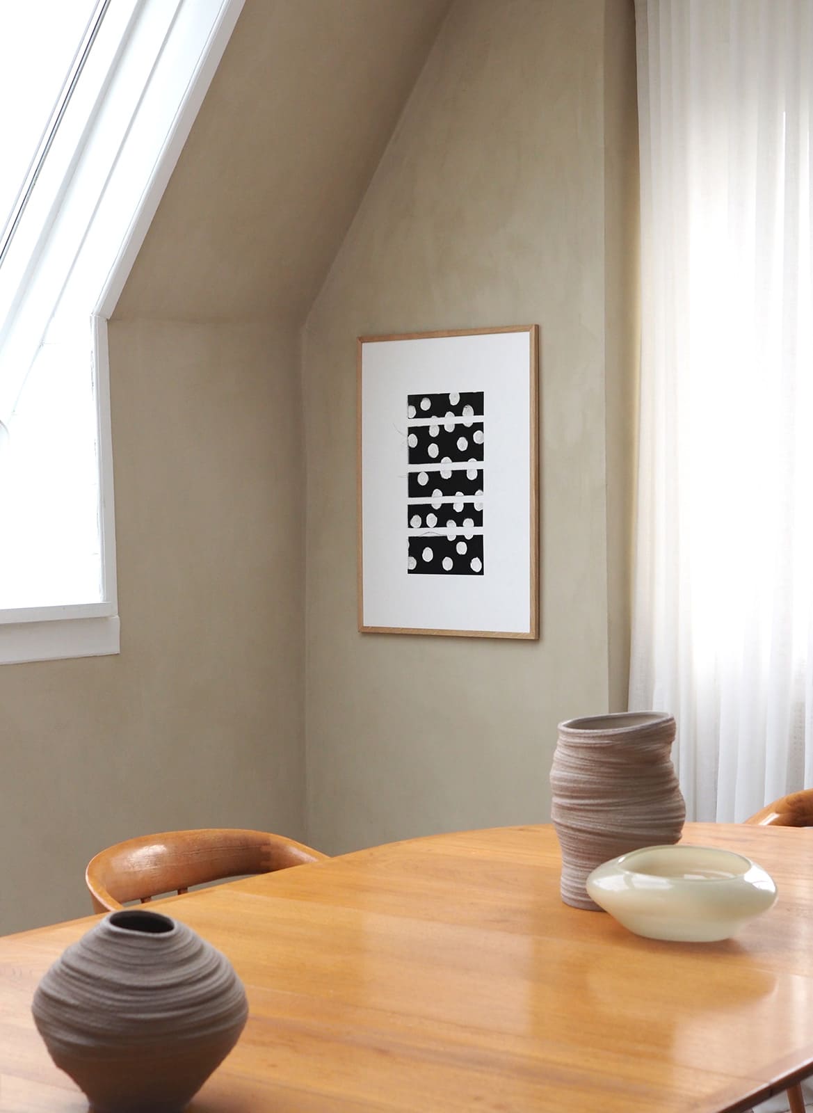 Framed white poster with dots hanging above a table by atelier cph