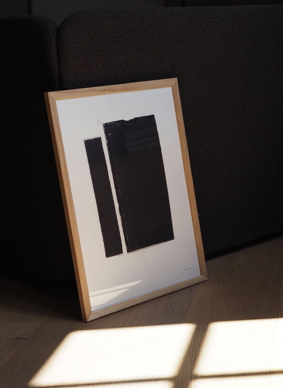Framed black and white poster standing against a couch by Atelier Cph