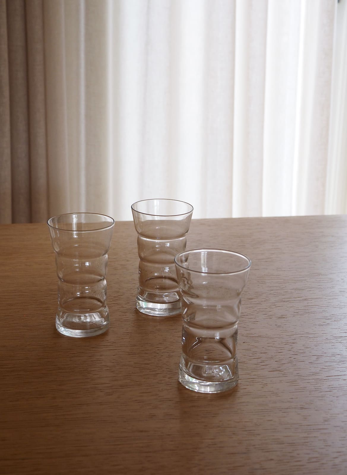 3 drinking glasses standing on a wooden table