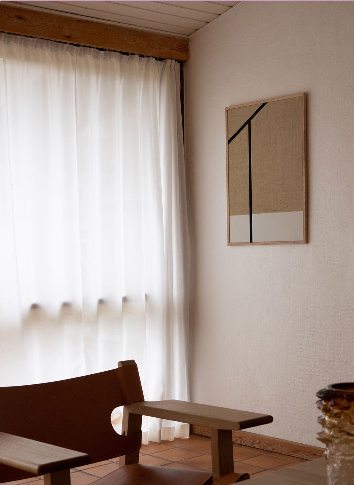 Framed minimalistic sandy poster with black lines hanging above a chair by atelier cph