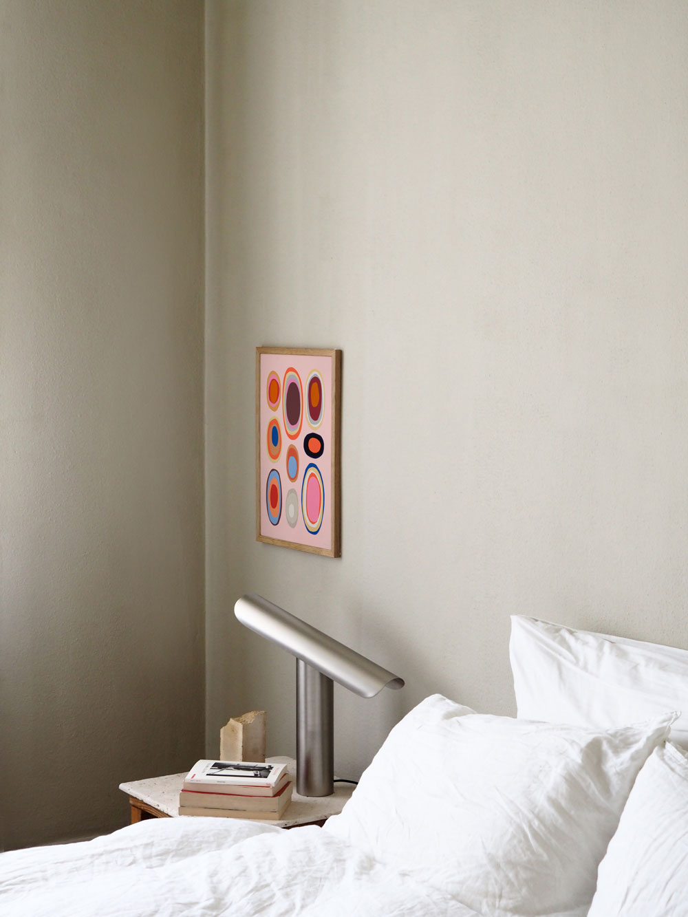 Framed colorful poster hanging above a bed by Atelier Cph