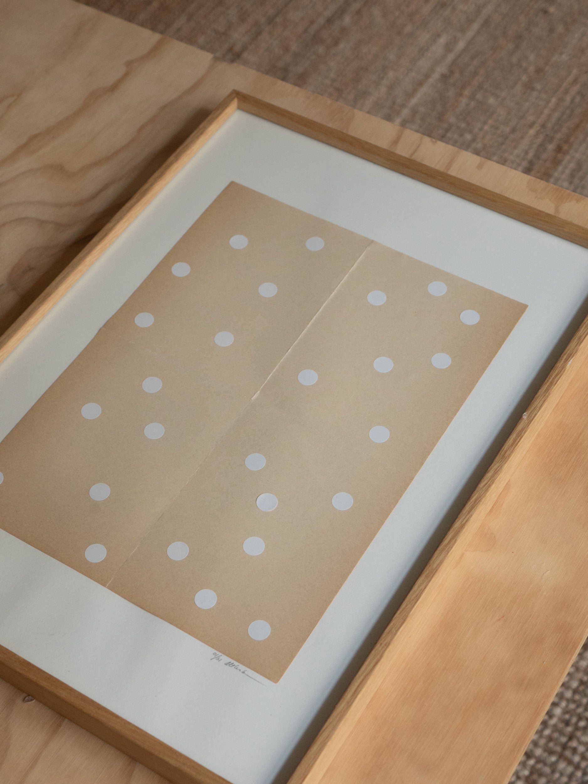Framed artwork with polka dot pattern in a oak wood frame on a wooden surface