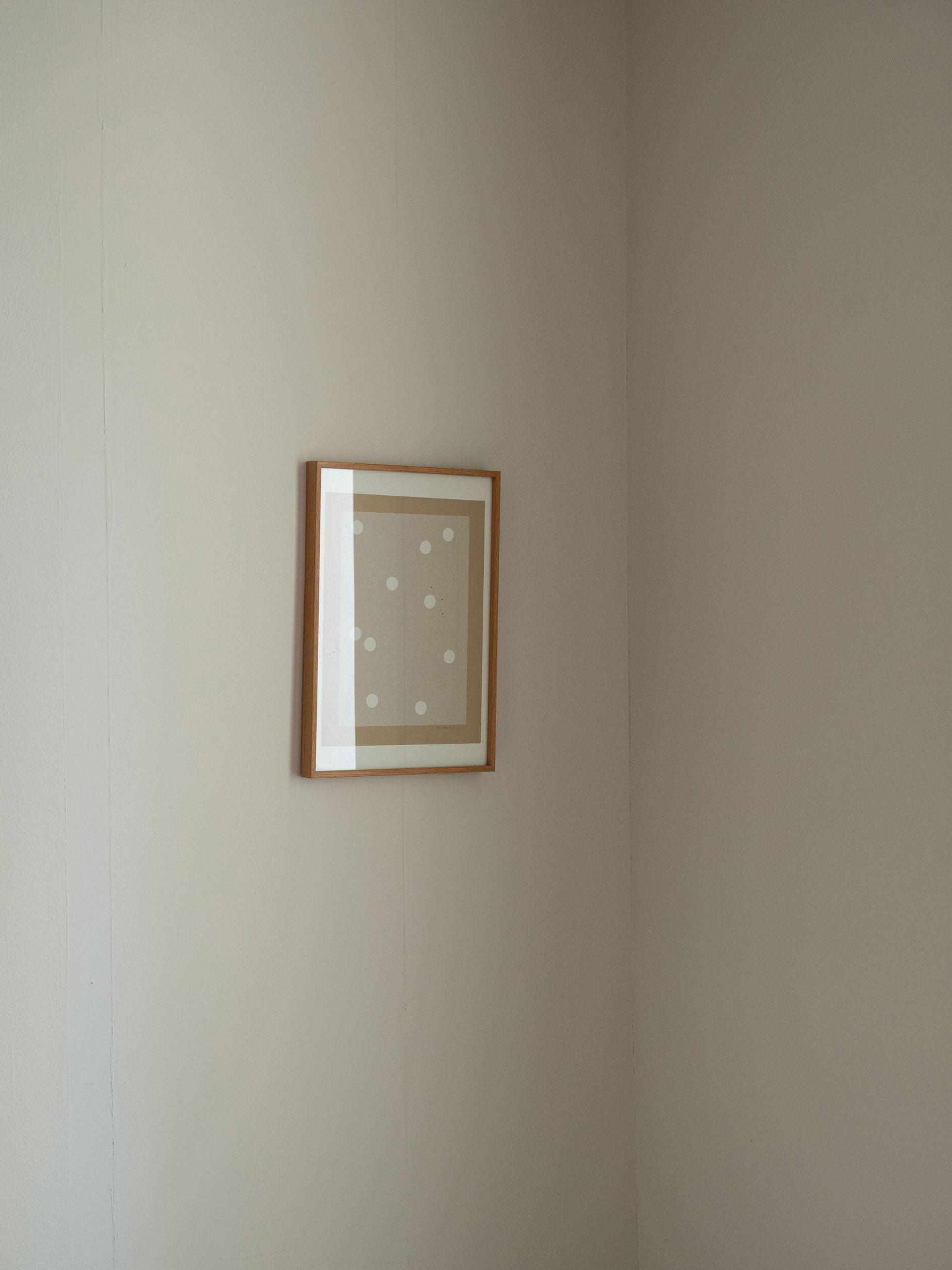 Minimalist sand-coloured artwork with white dots on textured folded paper, framed in solid oak, created as a limited edition by Atelier Cph on plain wall.