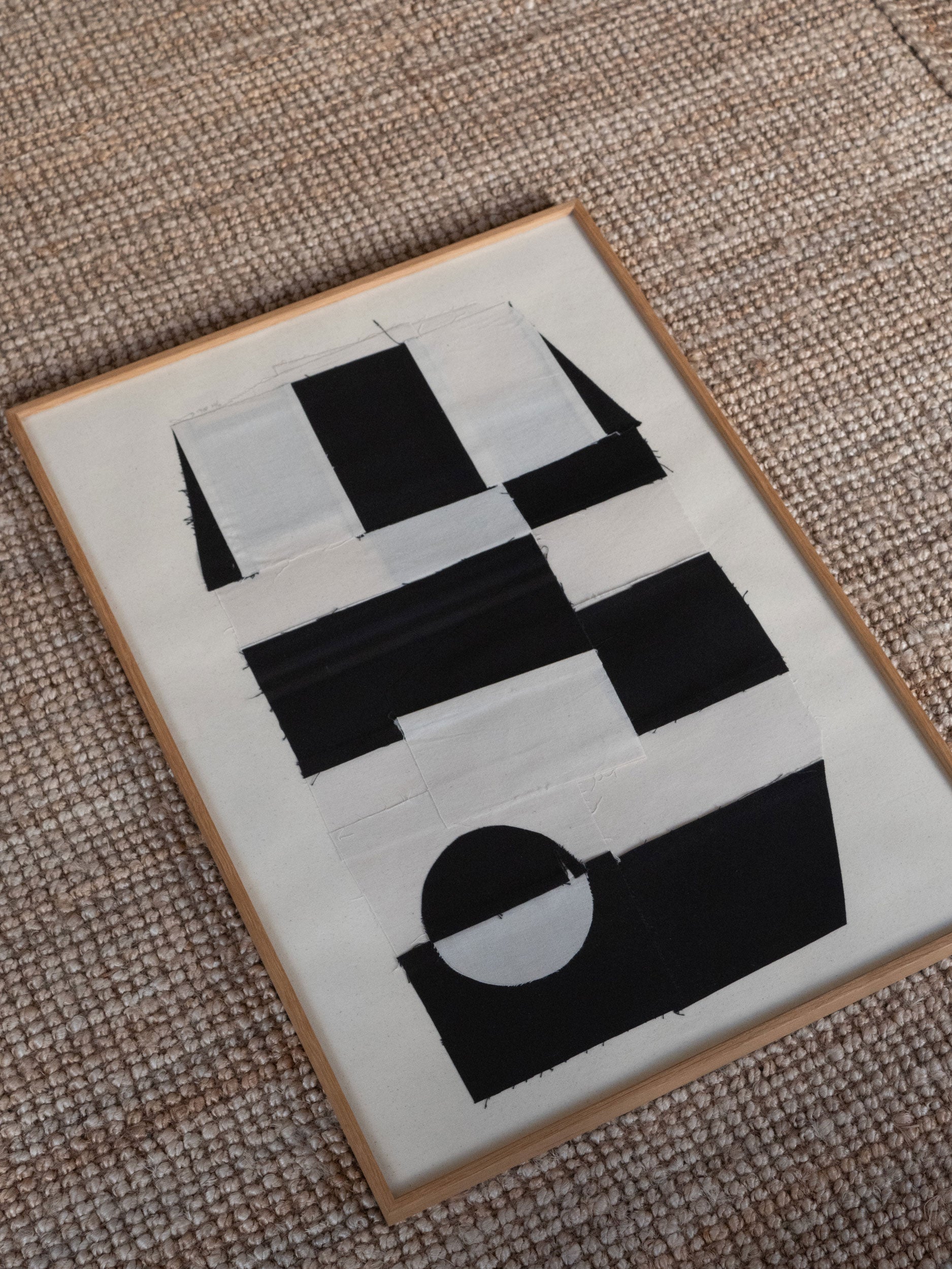 Black sewn geometric shapes on a white background in a wooden frame by atelier cph on a textured surface