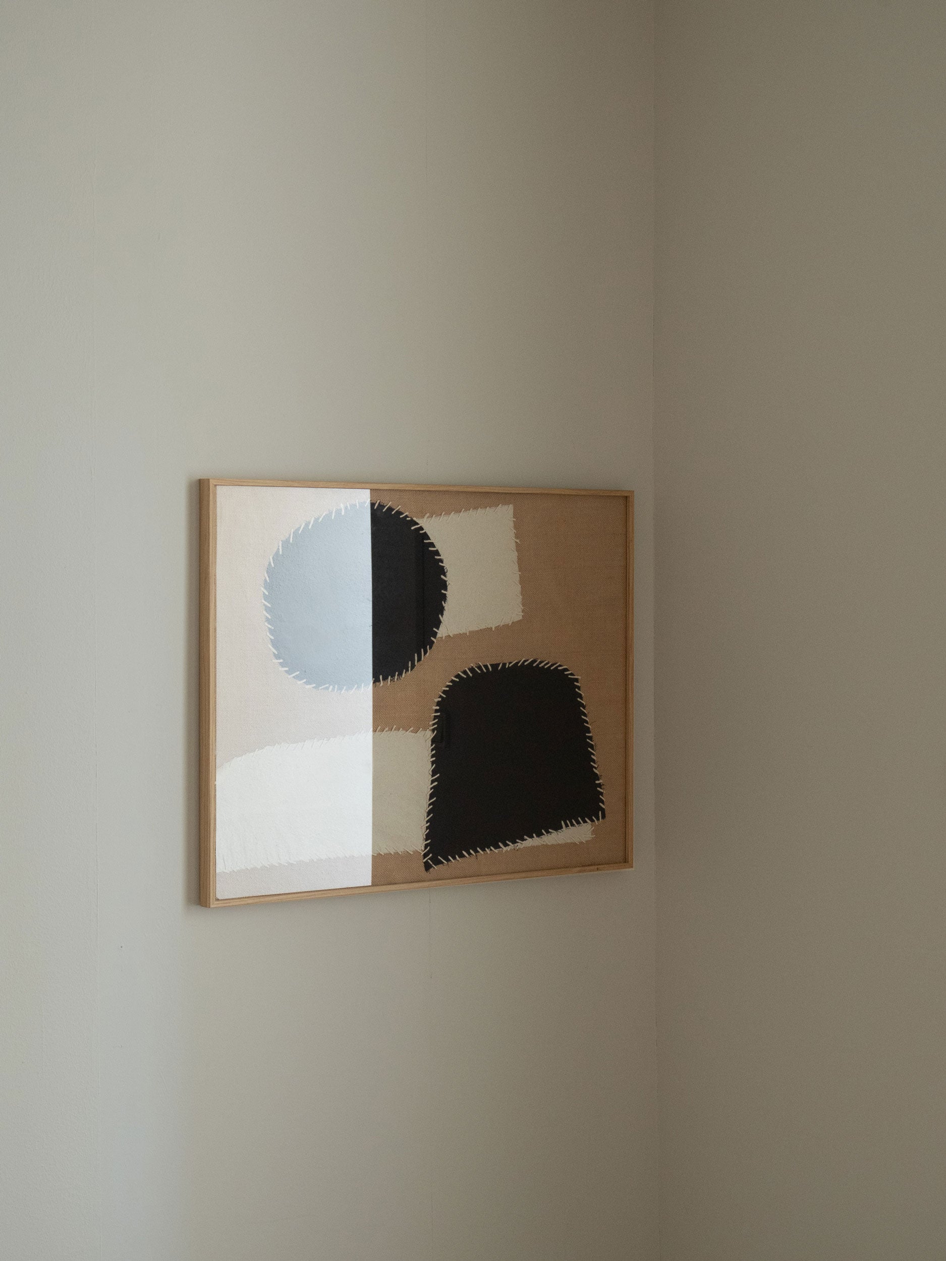 Minimalist textile artwork with black and white abstract fabric shapes on a hessian background, framed in oak, created as a limited edition by Atelier Cph