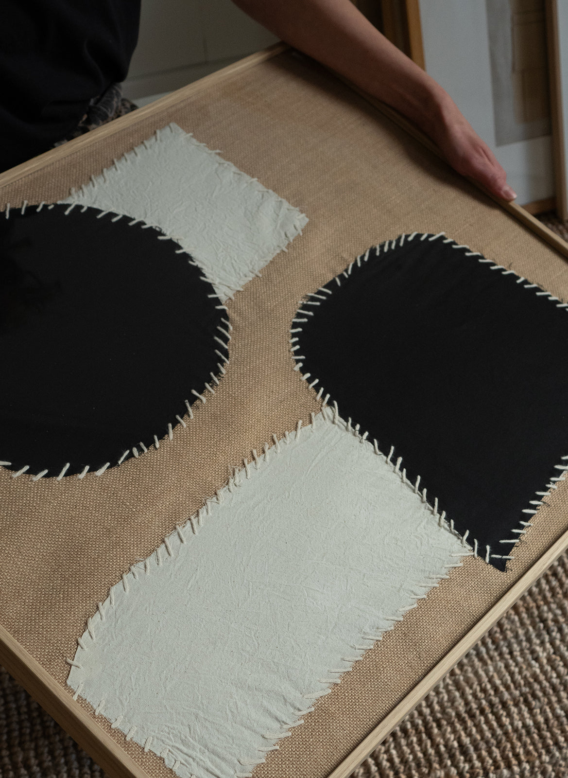 Minimalist textile artwork with black and white abstract fabric shapes on a hessian background, framed in oak, created as a limited edition by Atelier Cph