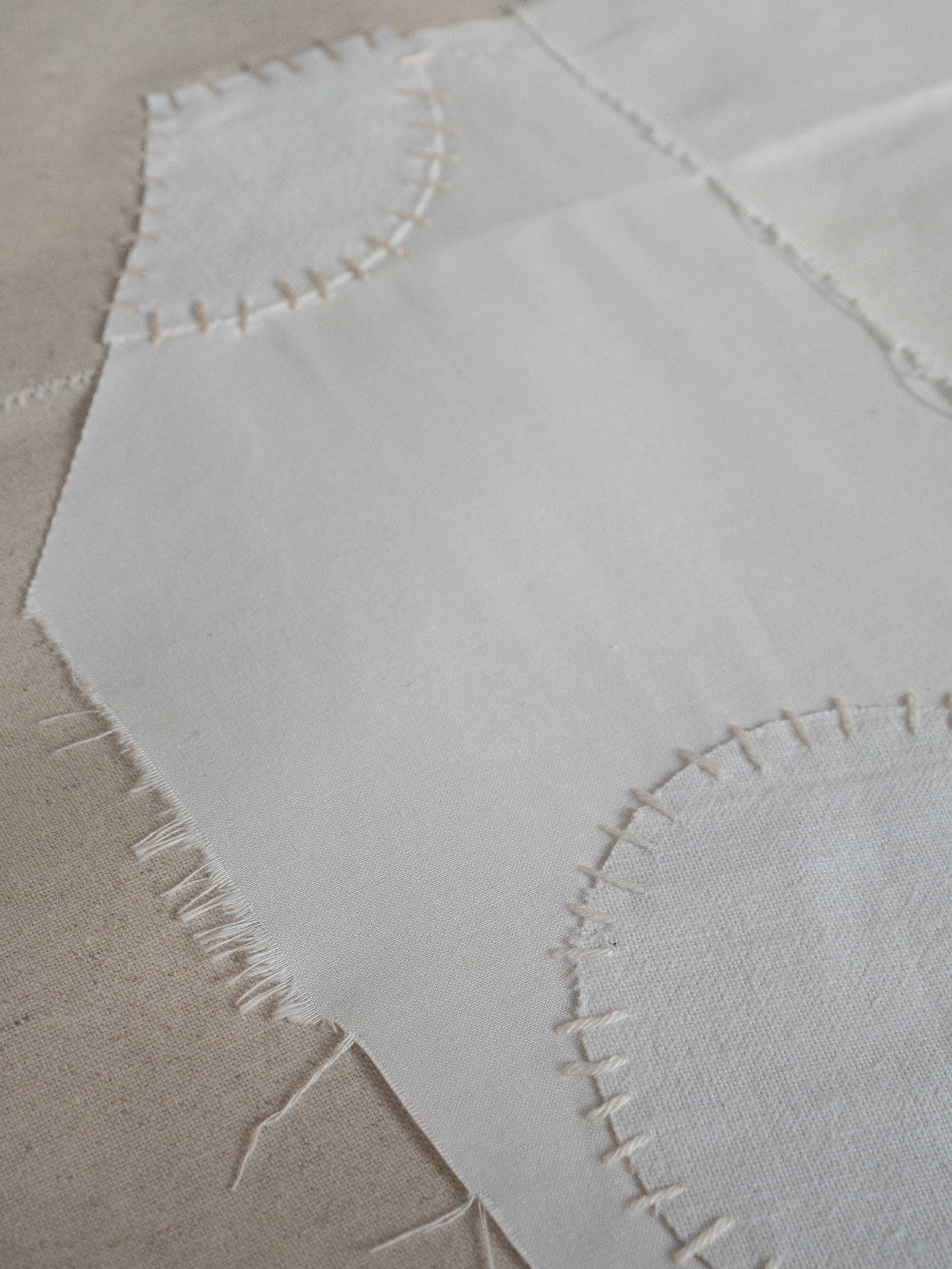 Close-up of a white fabric with embroidered patterns on a sandy background by Atelier Cph