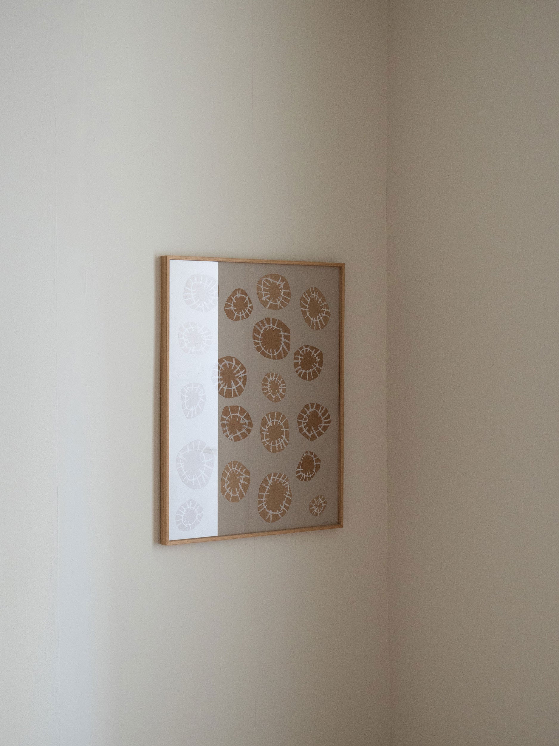 Minimalist artwork with sand-coloured circular shapes and white linear details on a grey background, framed in light oak, created as a limited edition by Atelier Cph on a beige wall.