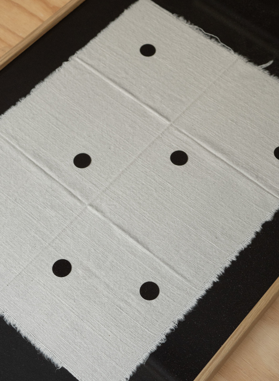 Minimalist black artwork with sand-coloured fabric and black dots, featuring frayed textile edges on a dark background, created by Atelier Cph as a limited edition art piece.