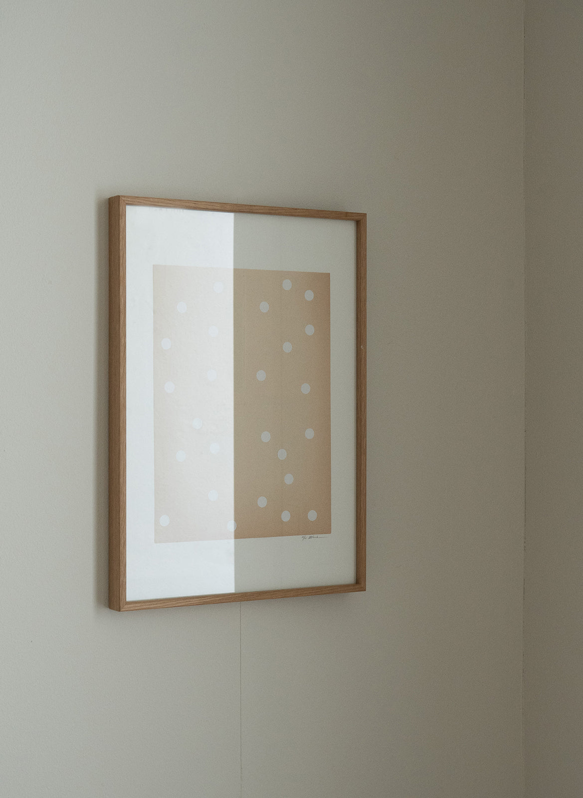 Framed artwork with polka dot pattern in a oak wood frame on a plain wall