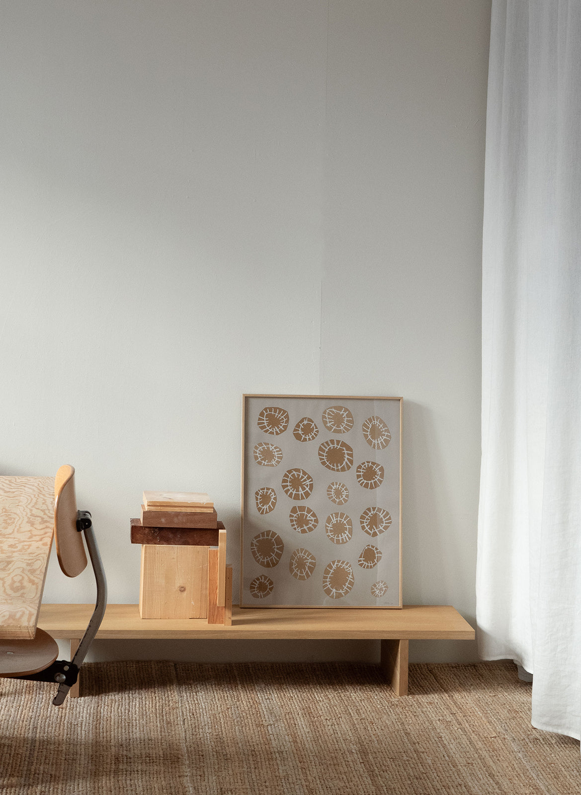 Minimalist artwork with sand-coloured circular shapes and white linear details on a grey background, framed in light oak, created as a limited edition by Atelier Cph on a beige wall with curtains.