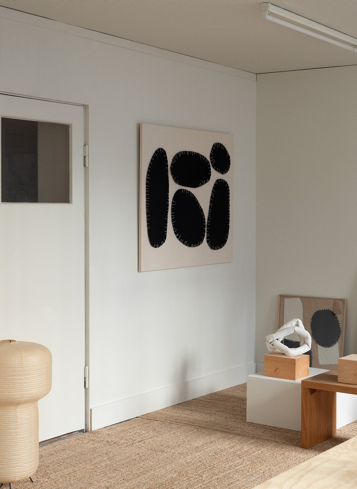 Minimalist textile artwork with large black organic fabric shapes outlined with white stitching on a sand-coloured background, created as a limited edition by Atelier Cph.