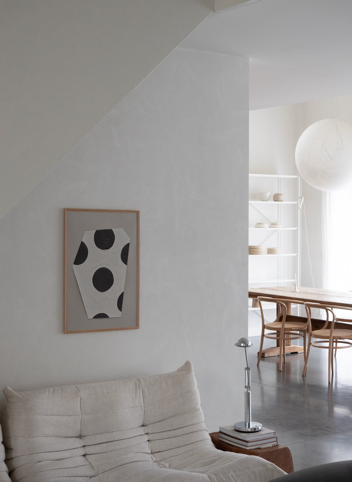 Modern living room with a sofa, abstract art on the wall, and a view into a dining area.