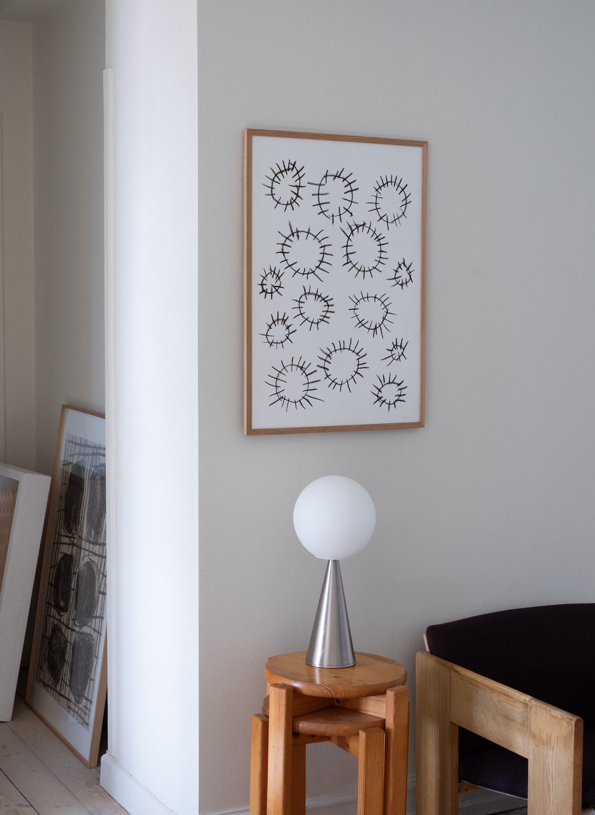 Framed abstract art on a wall with a lamp and stool in the foreground.