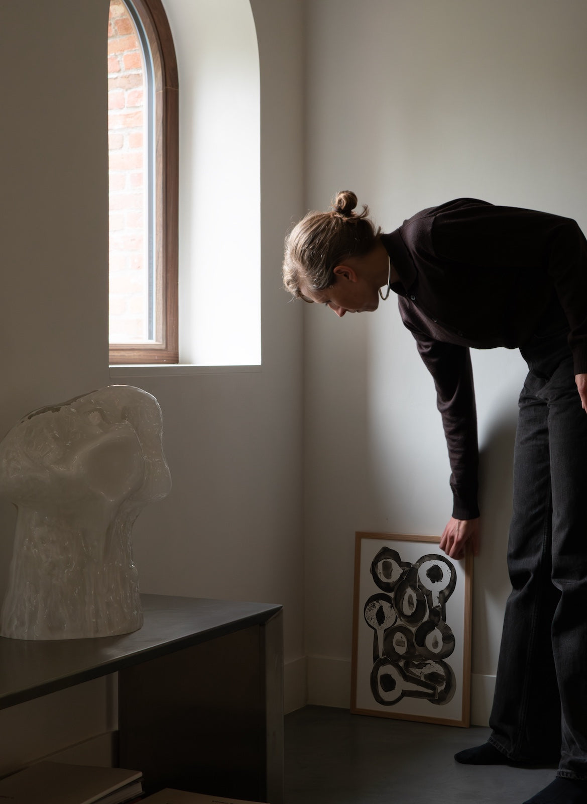 Person looking at a sculpture and artwork in a room with a window.