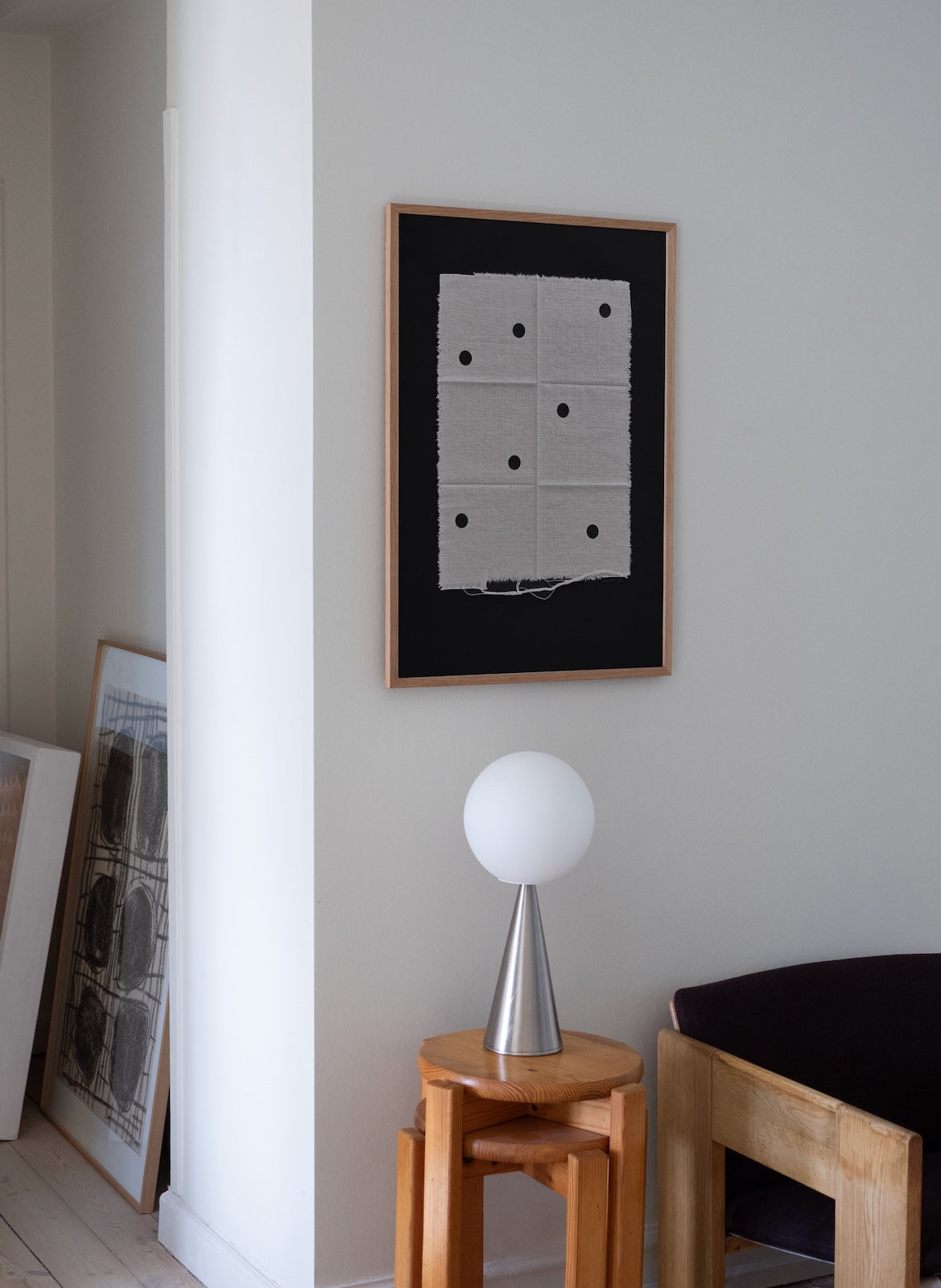 Framed artwork on a wall with a lamp and stool in the foreground