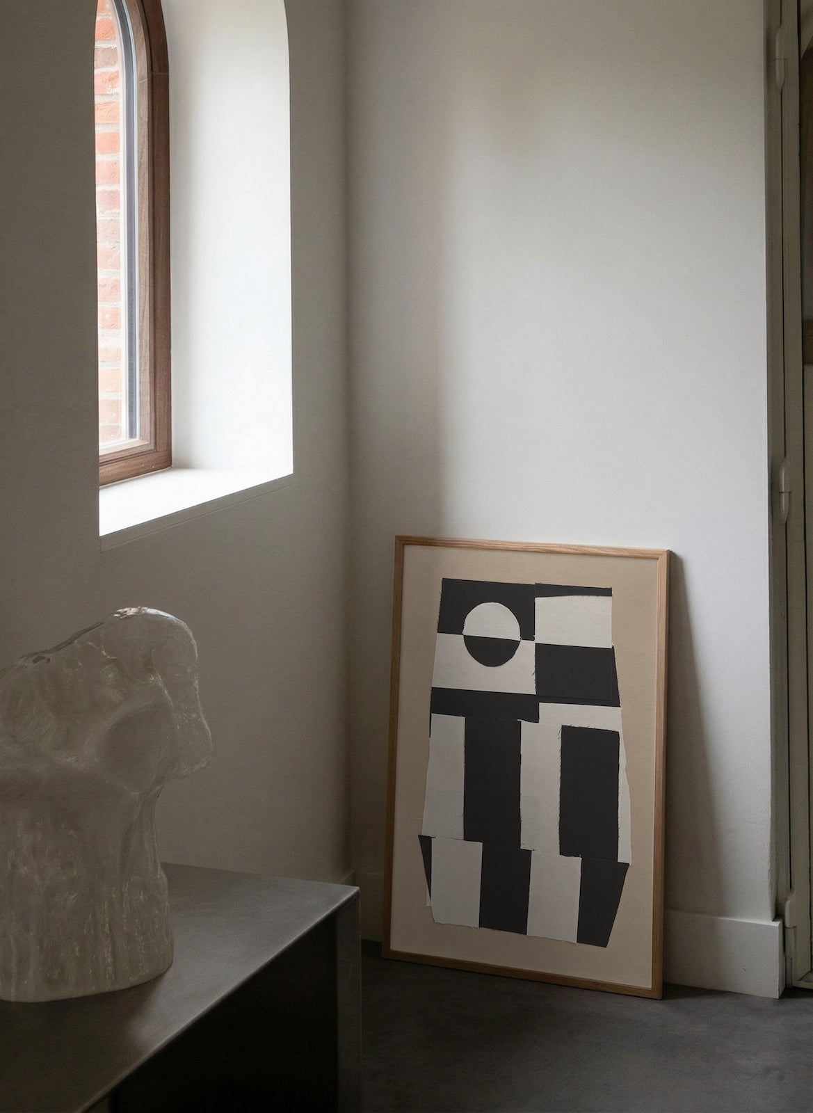 Framed abstract artwork leaning against a wall next to a window.