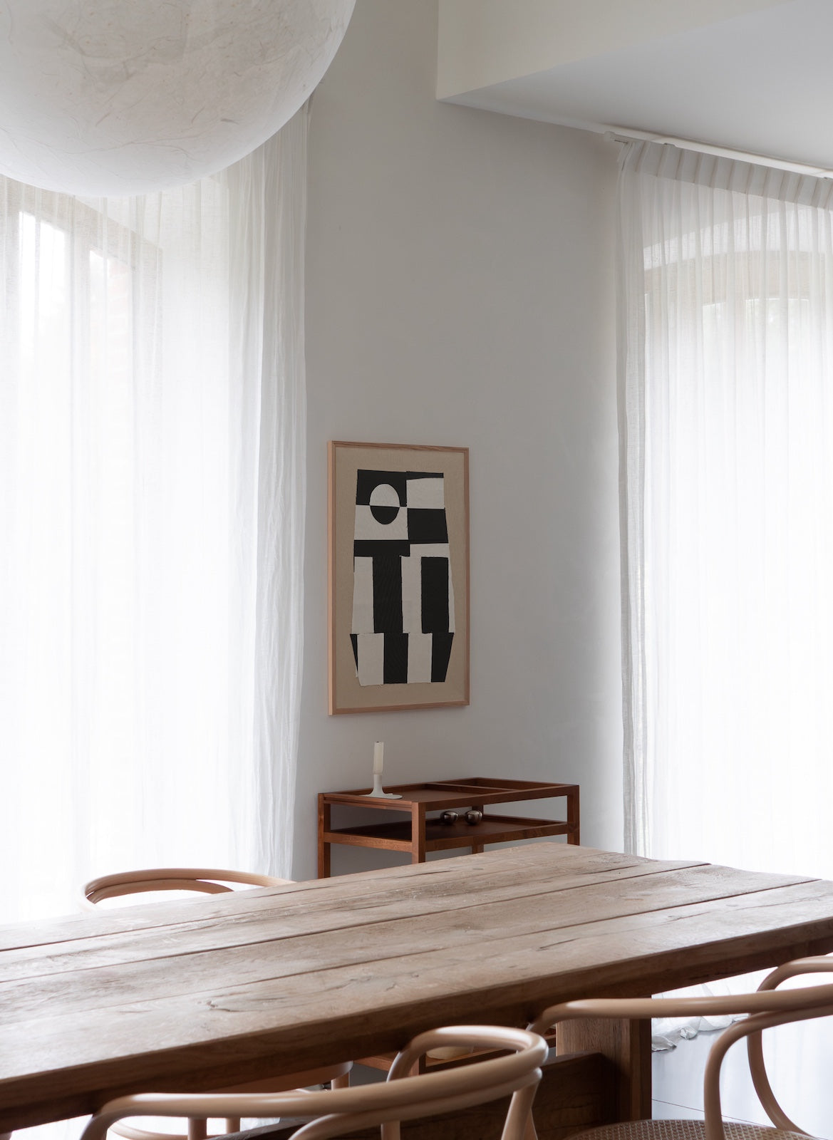 Modern interior with a wooden table and chairs, abstract art on the wall, and sheer curtains.