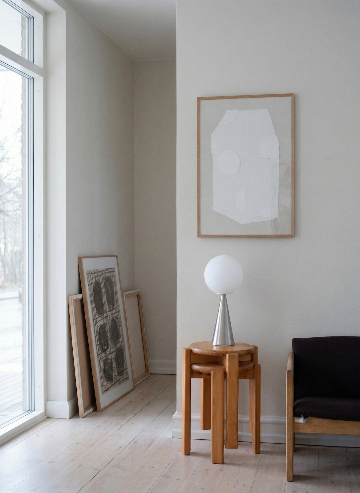 Modern interior with a lamp on a wooden side table, framed artwork, and a chair.