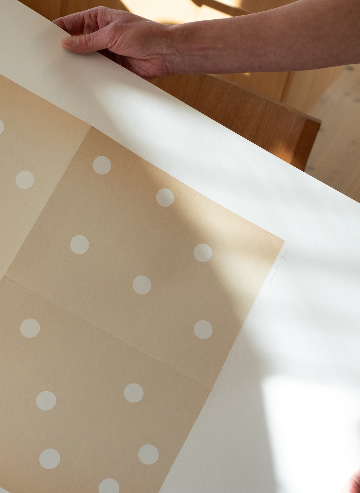 Beige paper with white polka dots being held by a hand