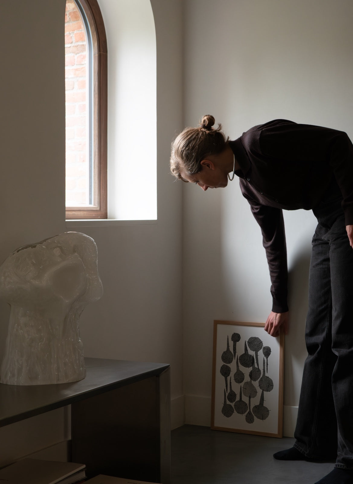 Person looking at a sculpture and artwork in a room with a window.