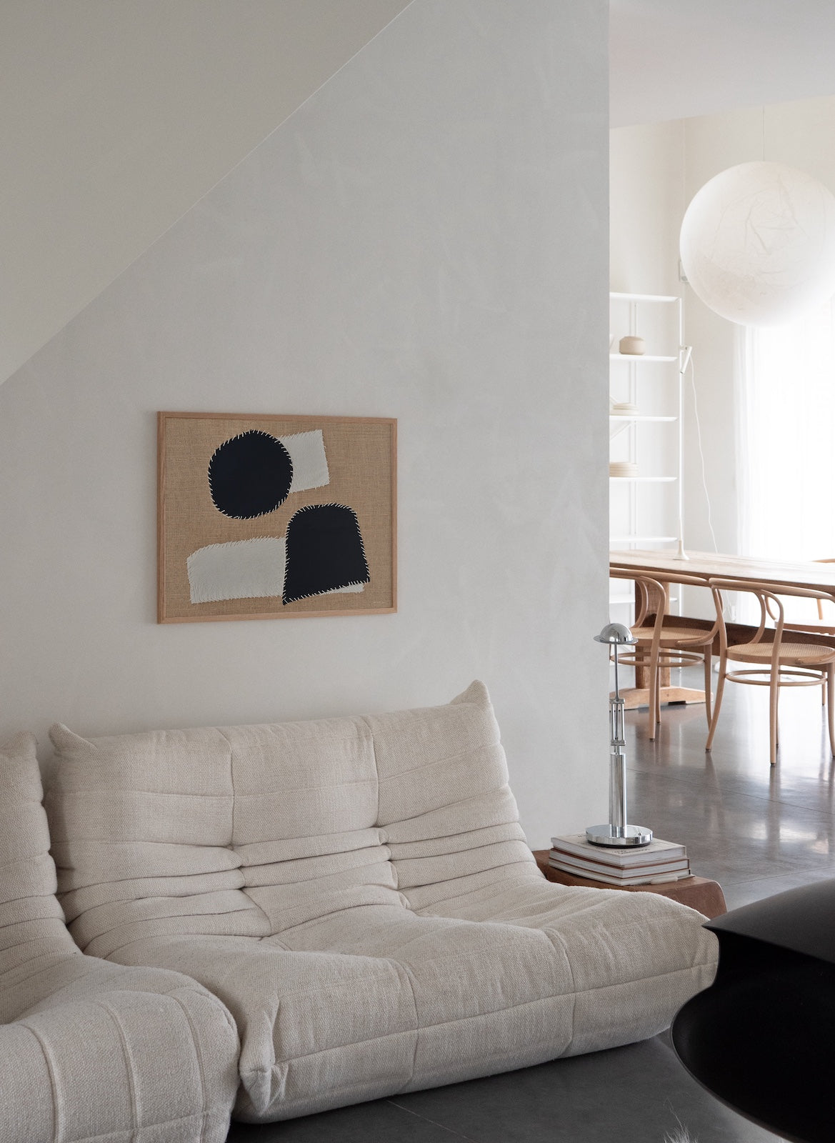 Modern living room with a beige sofa, abstract art on the wall, and a dining area in the background.