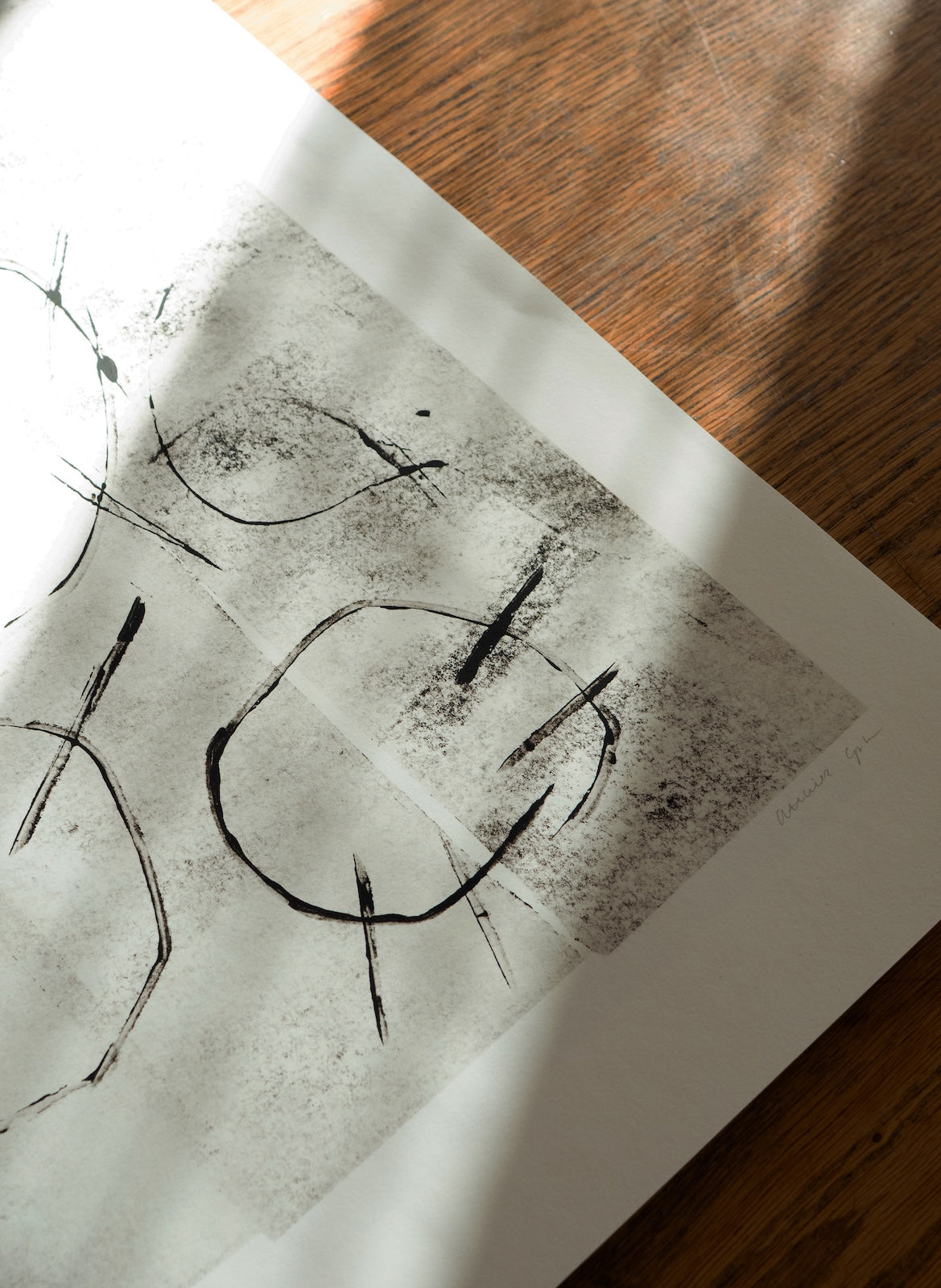 Black abstract line art on white paper with a wooden surface underneath