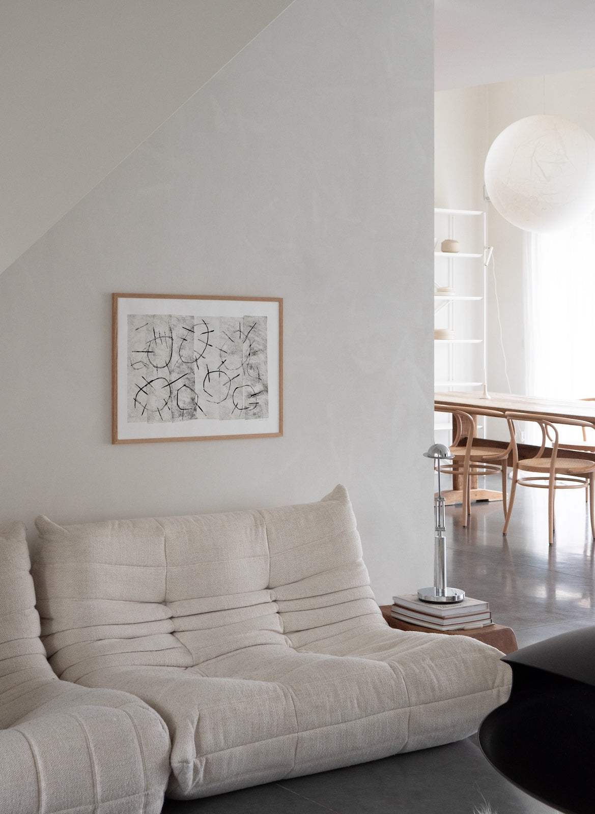 Modern living room with a beige sofa, abstract art on the wall, and a dining area in the background.