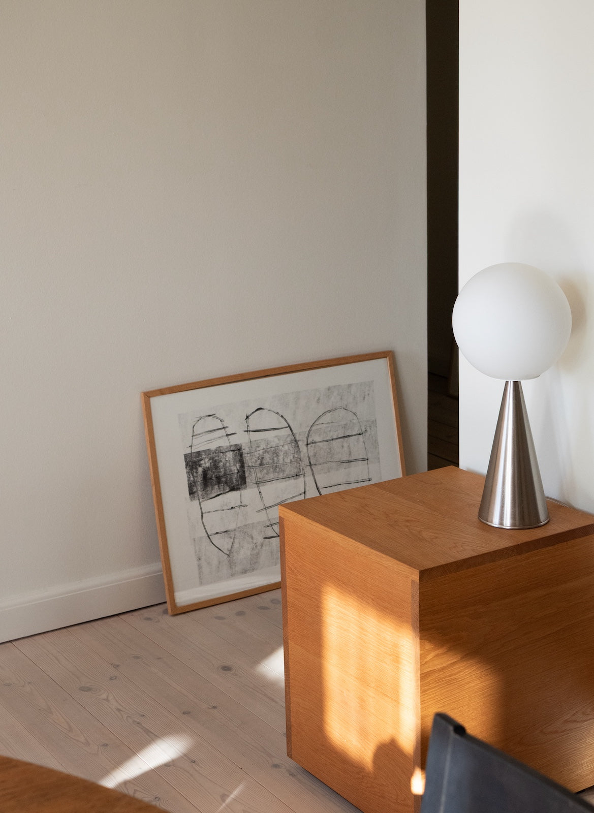 Framed artwork on a wall next to a wooden cabinet with a lamp on top.