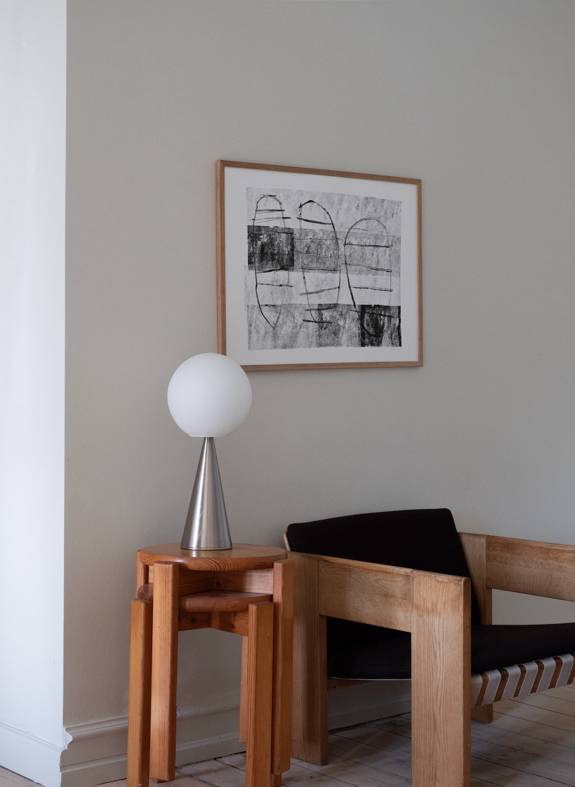 Wooden chair and side table with a lamp against a wall with framed abstract art.