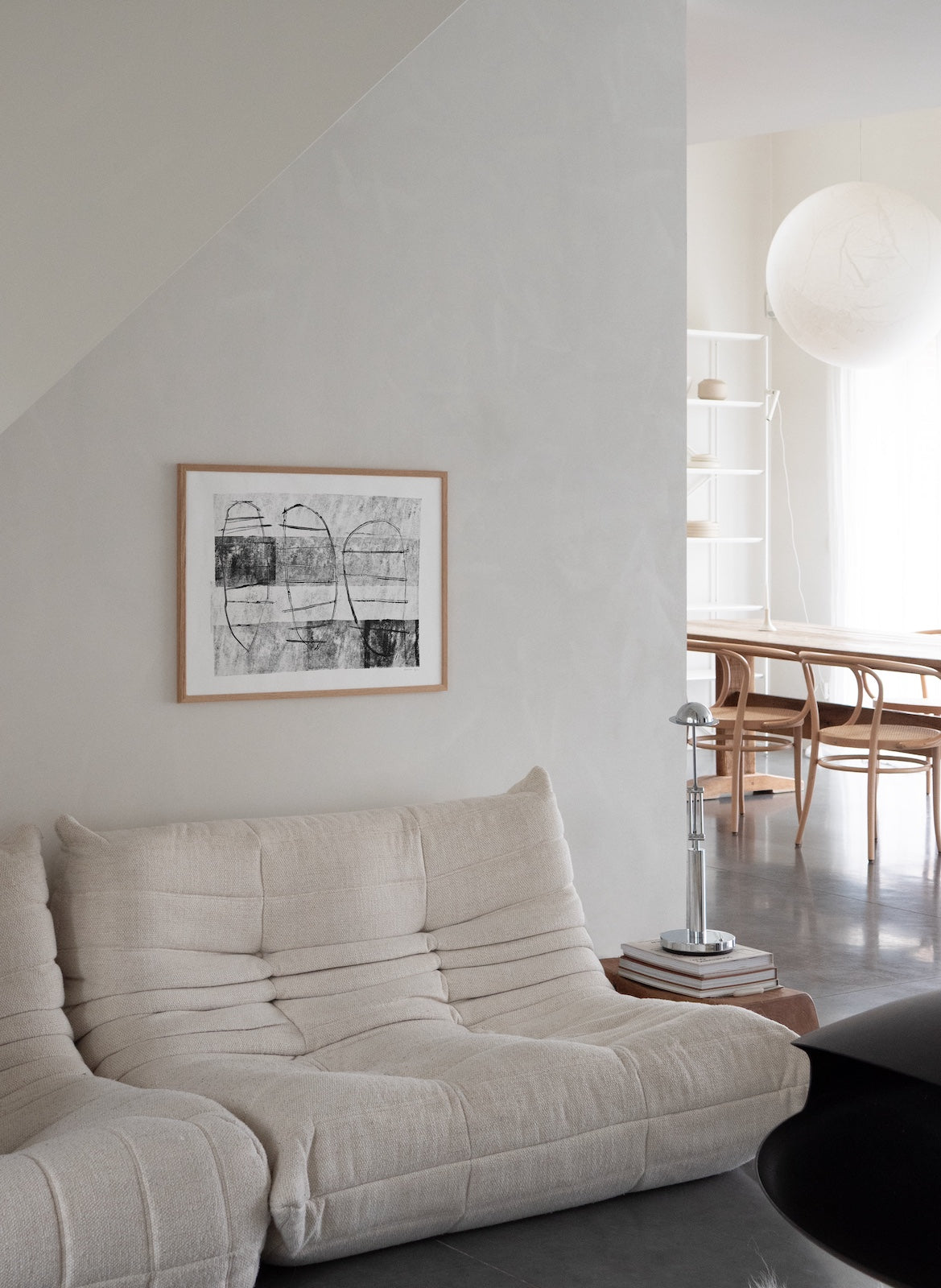 Modern living room with a beige sofa, framed artwork on the wall, and a dining area in the background.