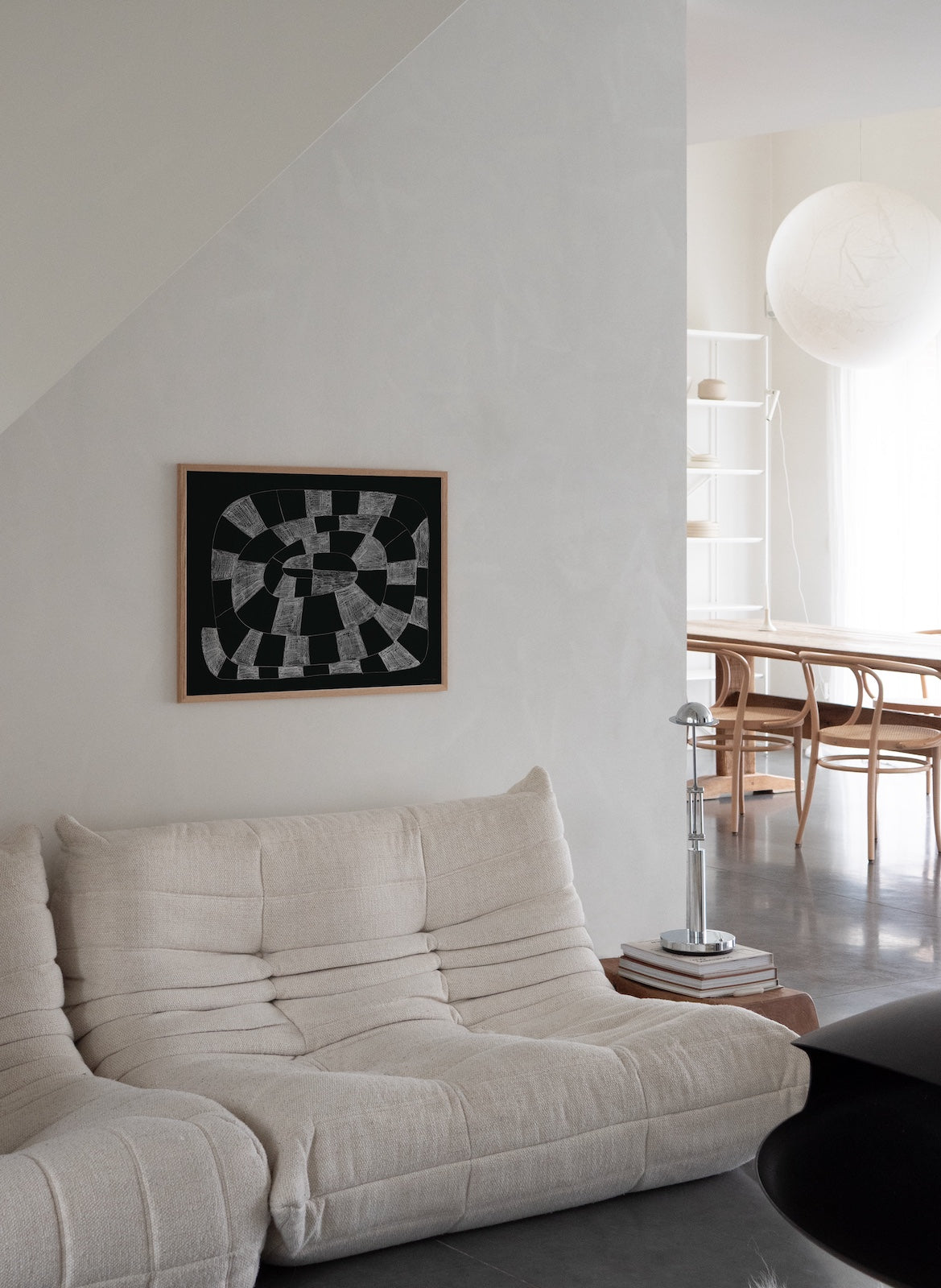 Modern living room with a white sofa, abstract art on the wall, and a dining area in the background.