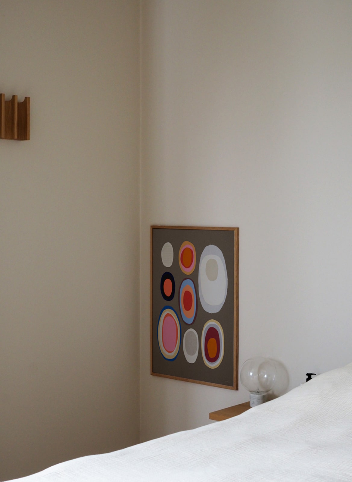 Framed colorful poster hanging next to a bed by Atelier Cph