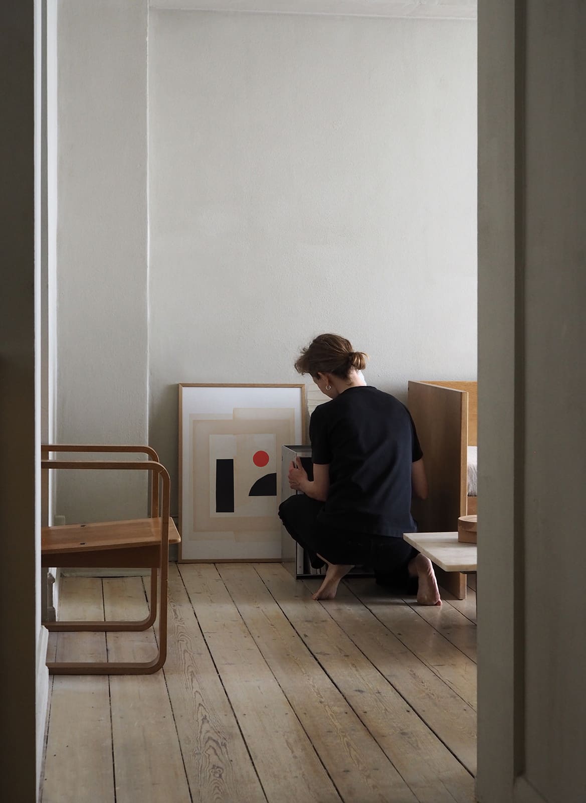 Framed minimalistic poster standing in a living room with a person by Atelier Cph