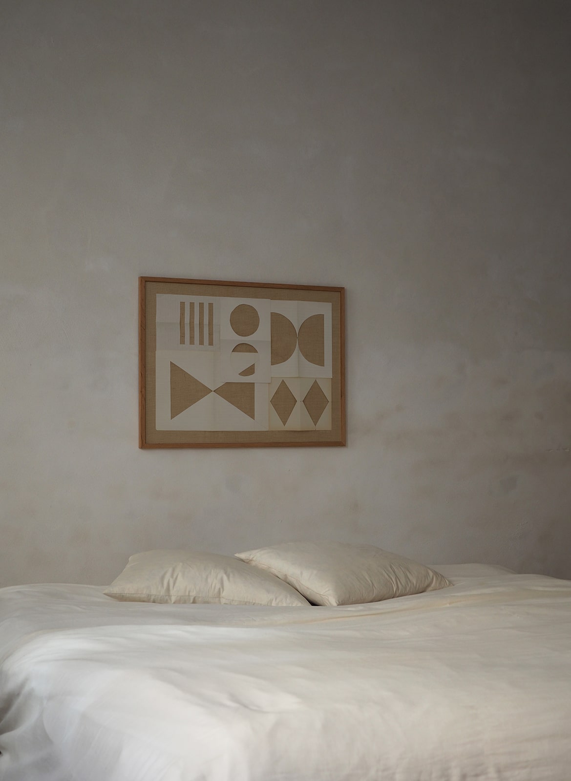 Framed art print with a paper cutout hanging above a bed by Atelier Cph