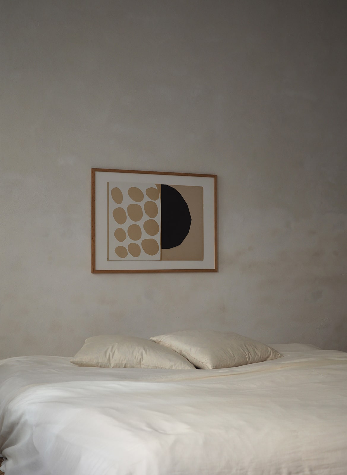 Framed poster with circles hanging above a bed by Atelier Cph