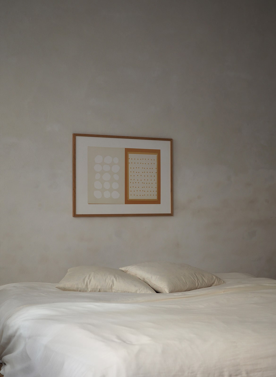 Framed poster with circles hanging above a bed by Atelier Cph