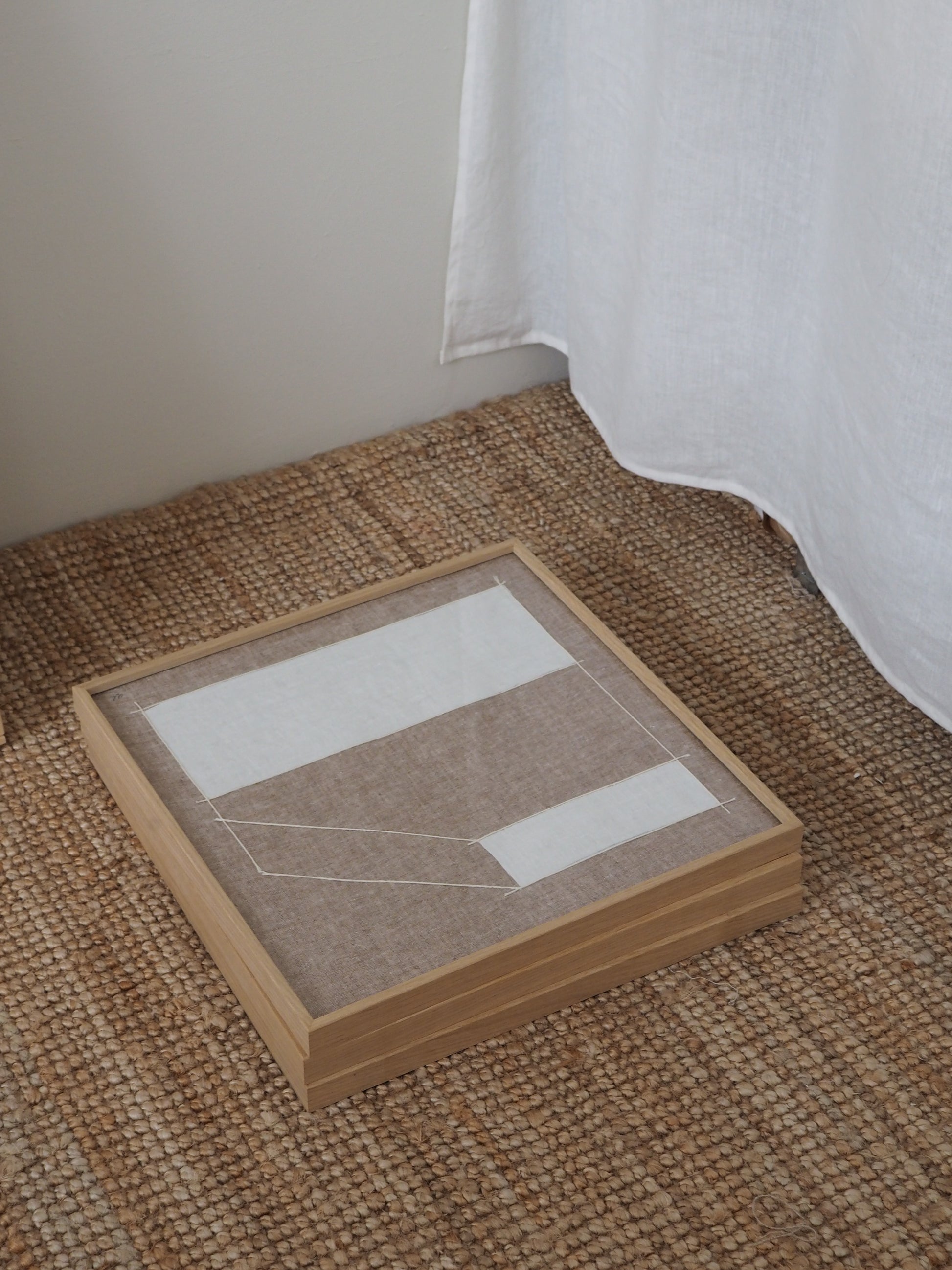 Abstract textile artwork made from natural linen with structured graphic lines in neutral tones laying on floor