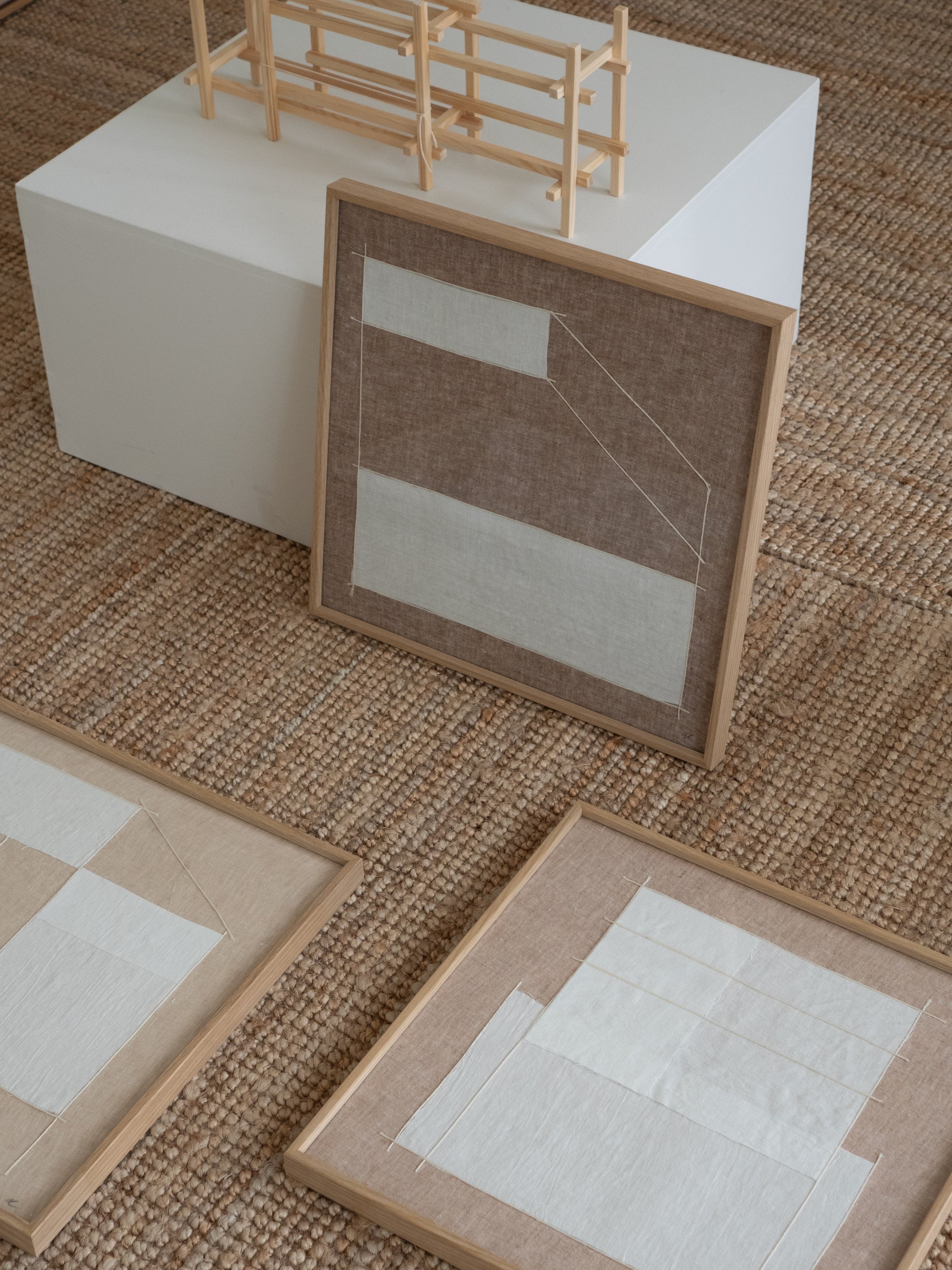 Minimalist textile wall pieces in natural linen featuring geometric line work and subtle variations in texture and tone laying on floor 