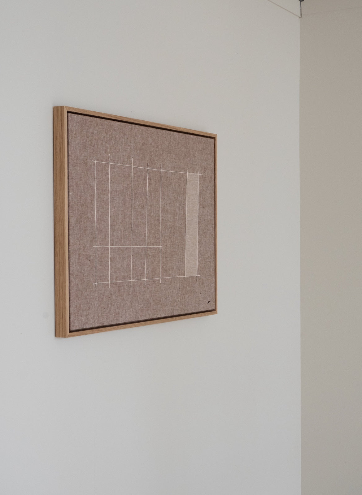 A square framed wall art piece with a beige textured center and a simple white geometric line drawing, mounted on a white wall.