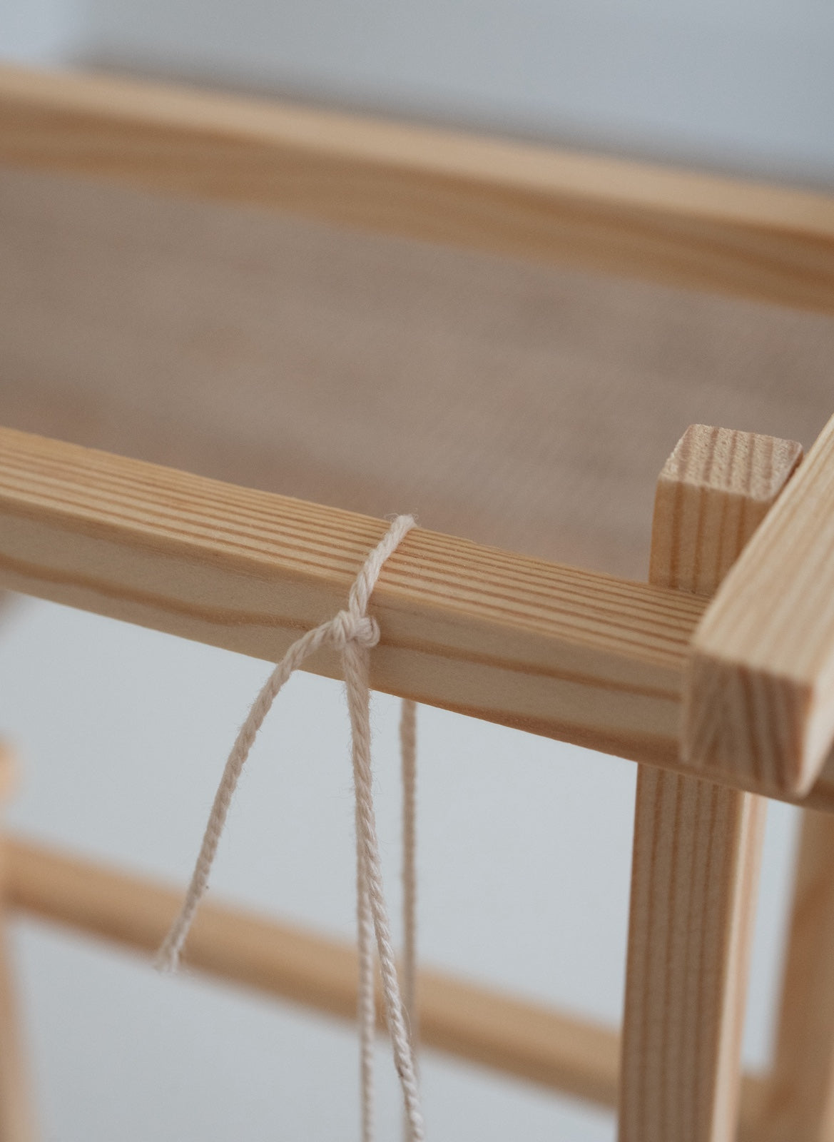 Close-up of a light natural wood frame with a white rope tied around one of the horizontal bars.