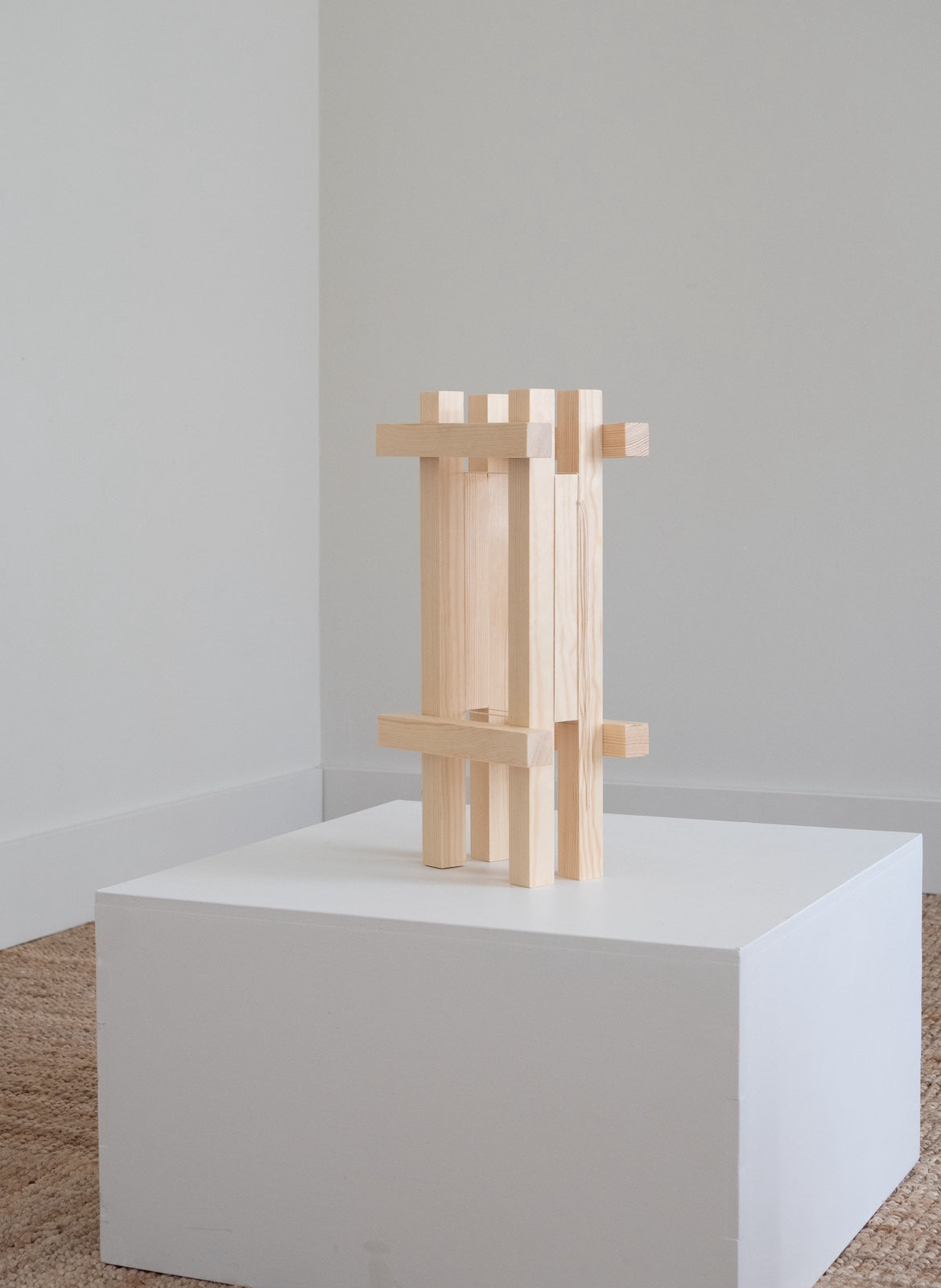 Architectural sculpture on podium made from wooden sticks on white box.
