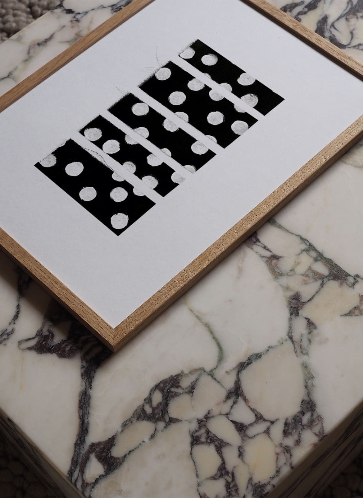 Framed white poster with dots laying on a marble table by atelier cph