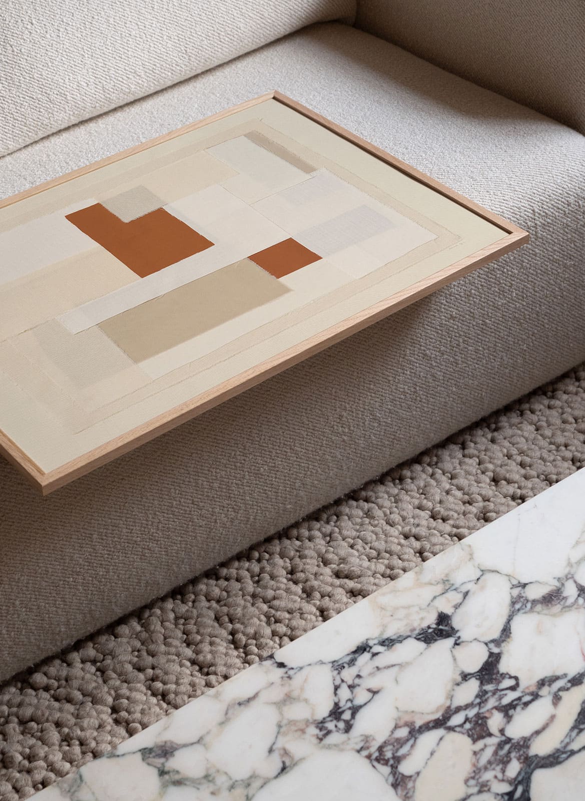 Framed beige poster laying on a couch by Atelier Cph