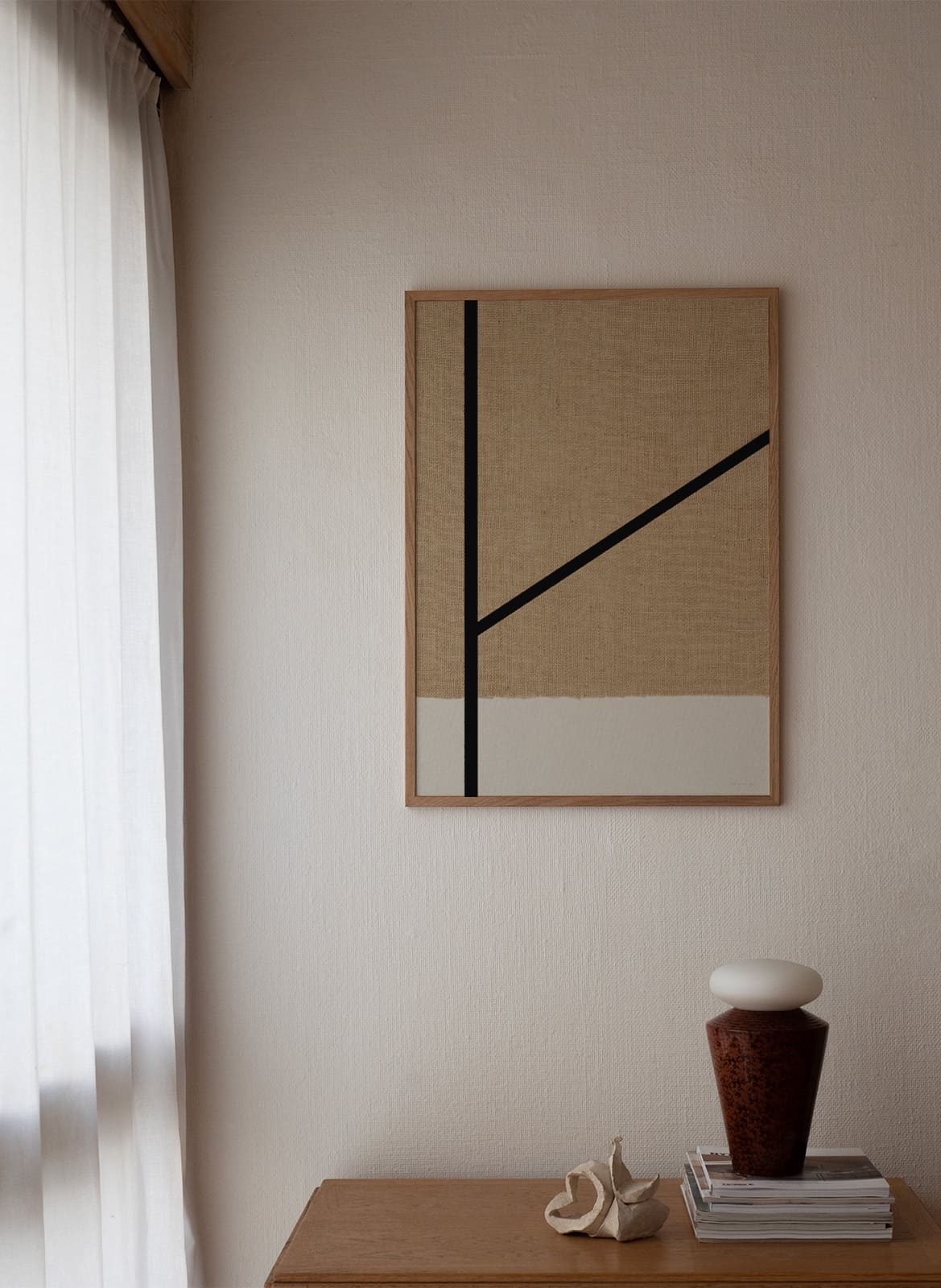 Framed minimalistic sandy poster with black lines hanging above a table by atelier cph