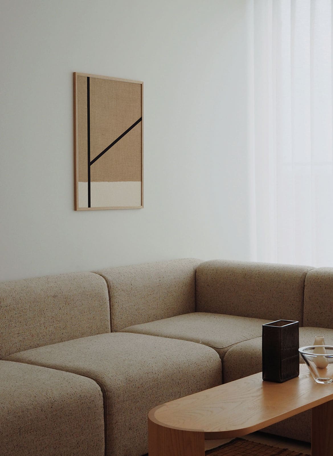 Framed minimalistic sandy poster with black lines hanging above a couch by atelier cph