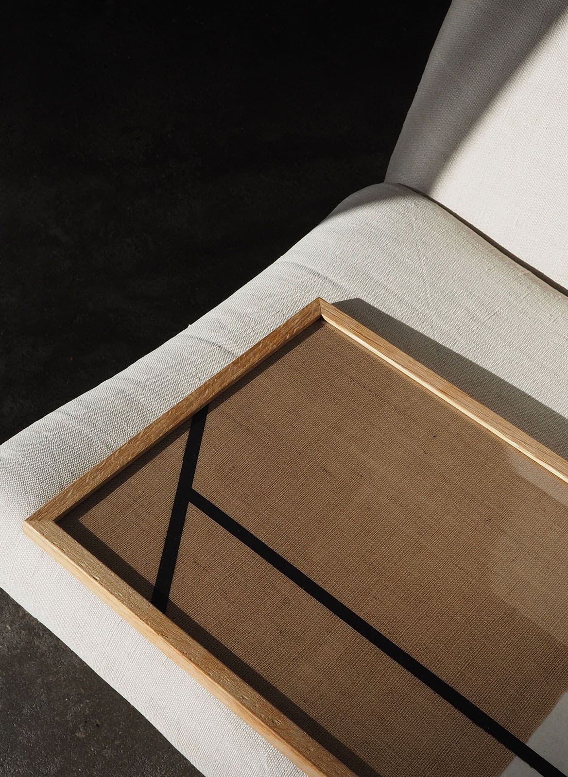 Framed minimalistic sandy poster with black lines laying on a chair by atelier cph