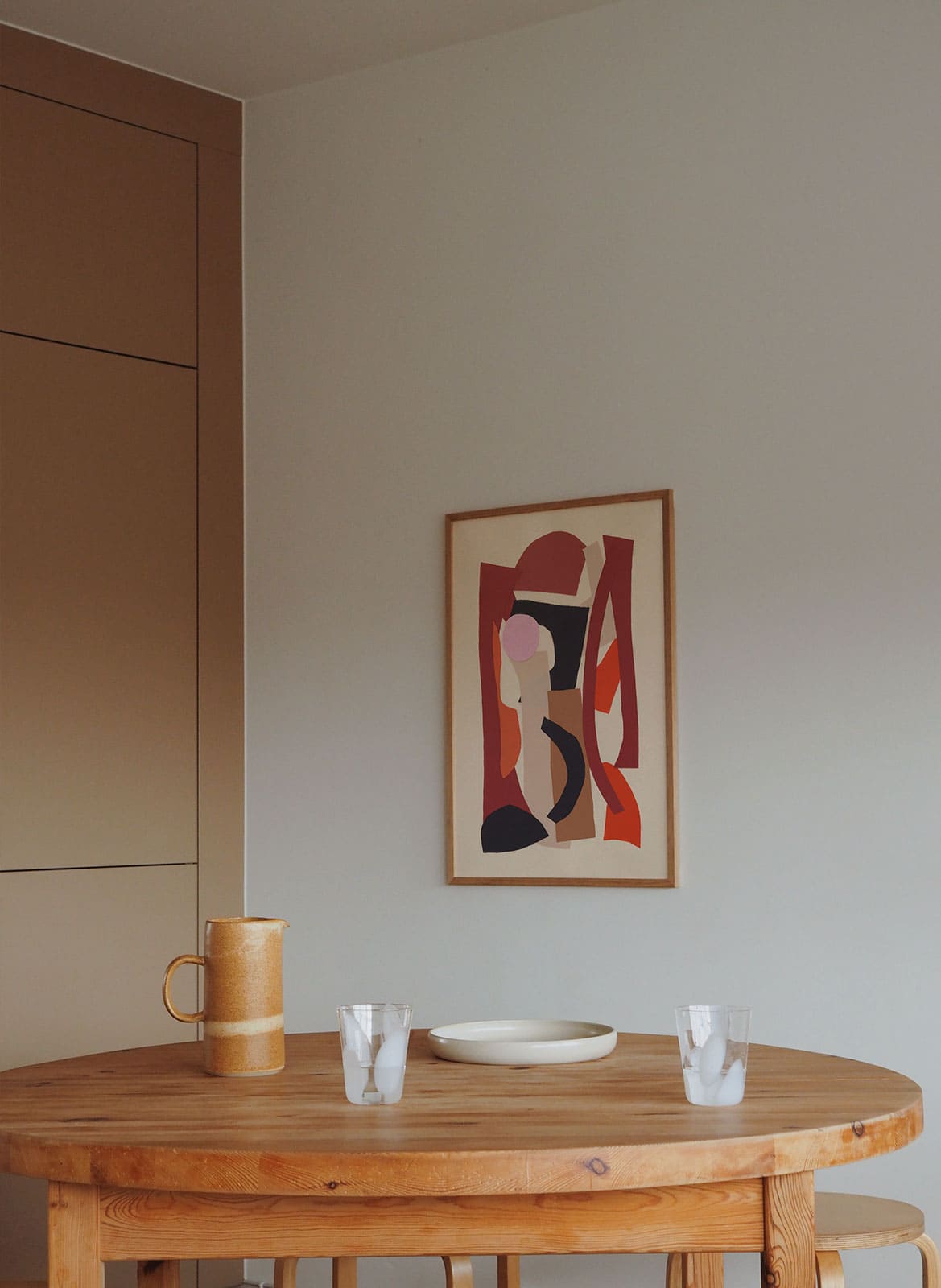 Framed colorful poster hanging above dining table by Atelier Cph